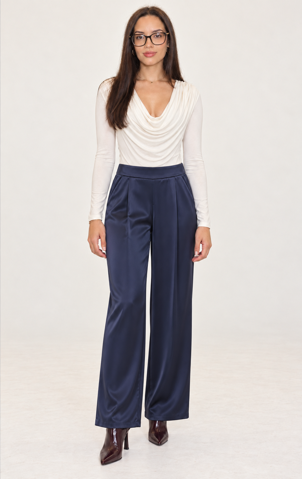 Modelo con body blanco drapeado, pantalón satinado azul marino y botines burdeos